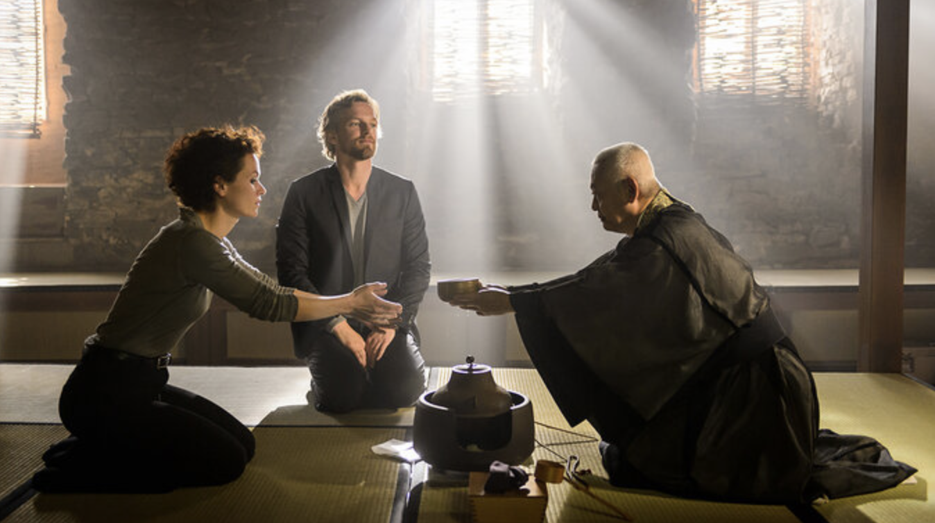 a monk hands overs a bowl to Louise